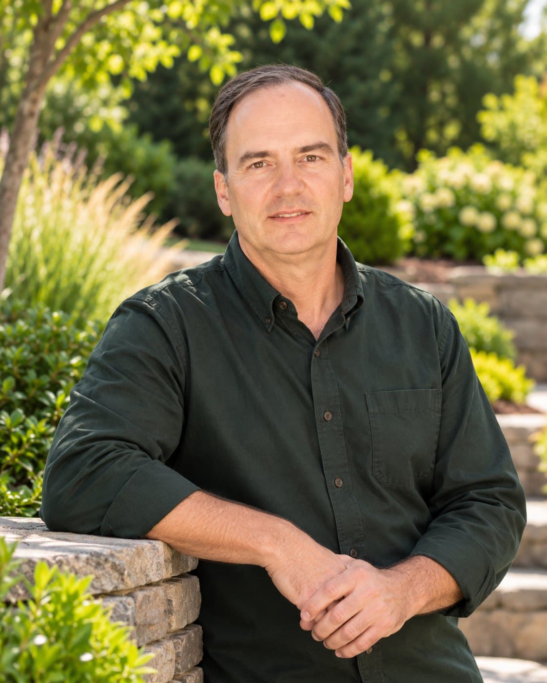 Chris Whitt leaning on a stone wall in a planted garden